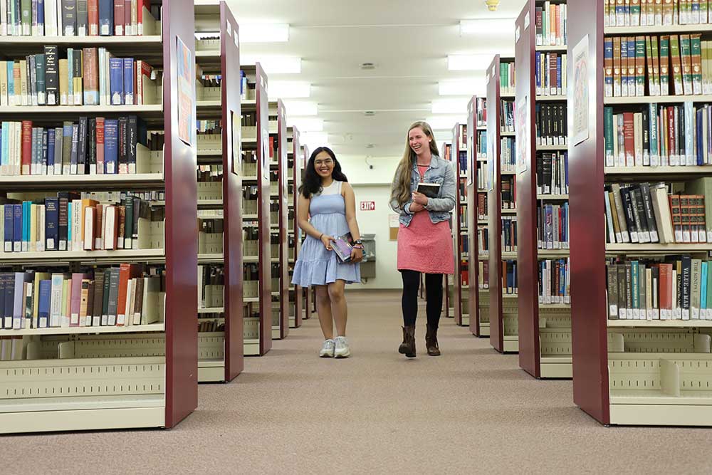 2 patrons walking down aisle surrounded by shelves of bbooks in archive